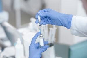 Gloved hands hold syringe to glass vial