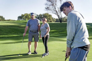 Rickey Malloy (left), who receives tofersen treatment for SOD1-ALS at WashU Medicine, plays a round of golf with his wife, Jenny, and their son, Kash.