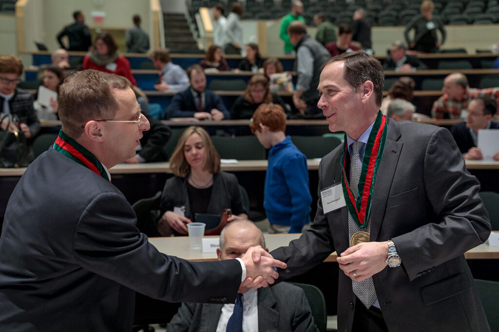 Beau Ances, MD, PhD (left) and Dan Brennan II shake hands after Ances' installation as the Daniel J. Brennan, MD, Professor of Neurology. The professorship is funded by a bequest from Brennan's father.