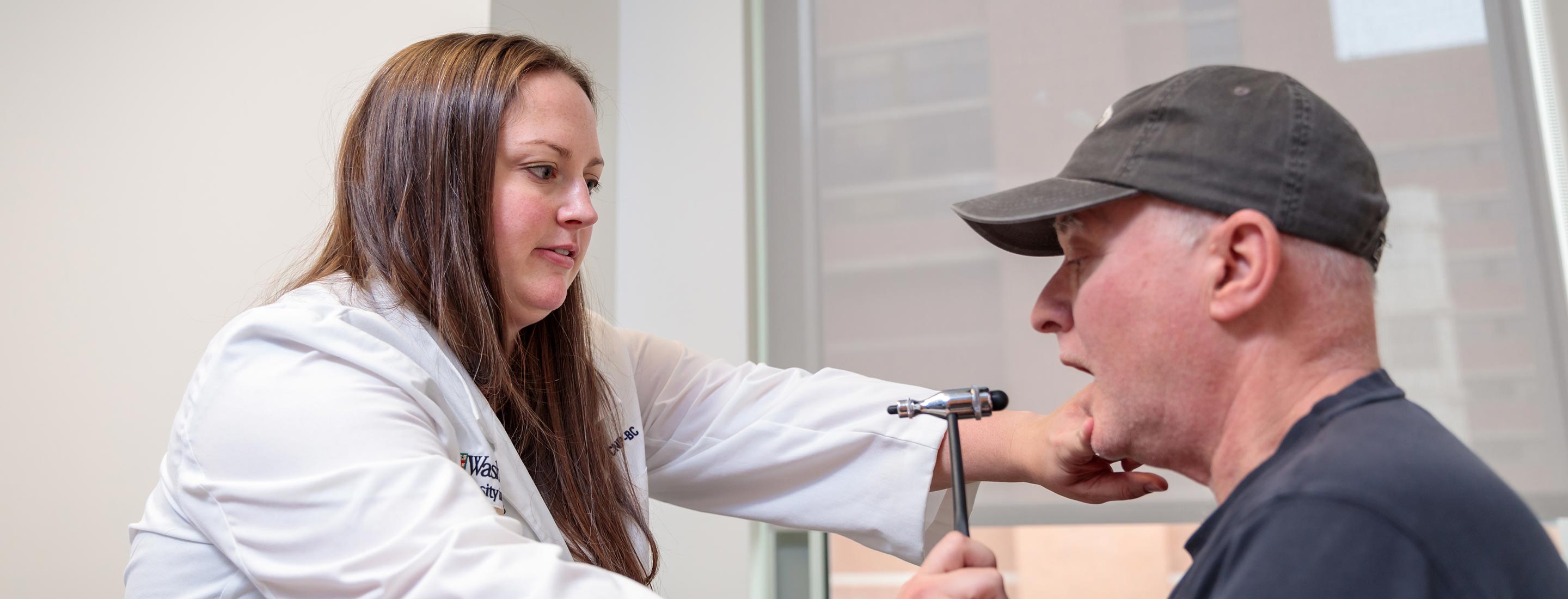 A physician examines a male patient wearing a baseball cap