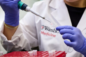 Person in lab coat uses a pipette and vial.